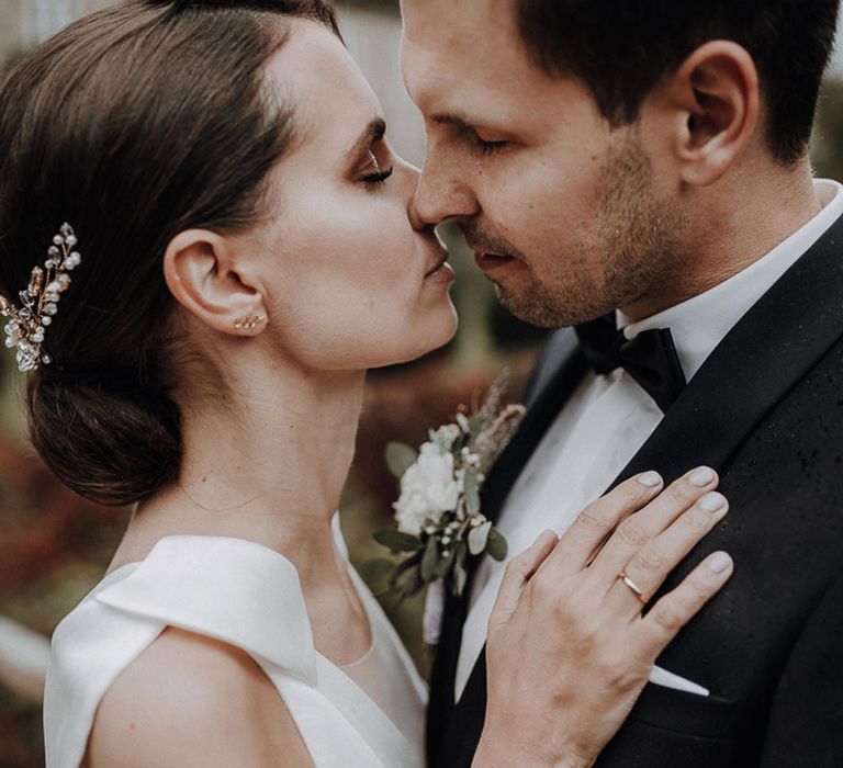 Bride in white Jesus Piero gown and cathedral length veil kisses groom in black Tiger of Sweden tux in gardens at German wedding with elegant details