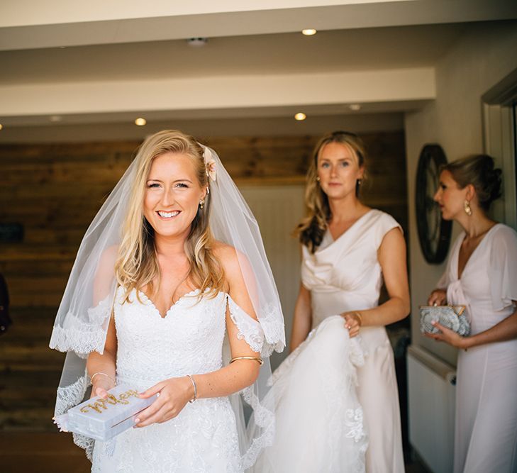 Bridesmaid holding brides lace wedding gown bride looking at the camera smiling holding gold and white wifey purse