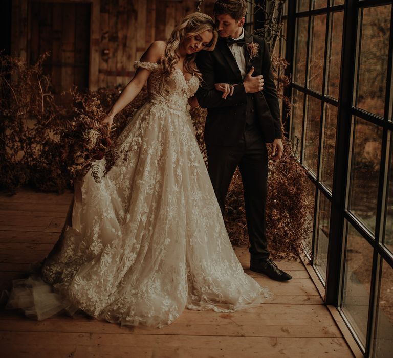 Bride in a Bardot wedding dress with lace detail standing at the Crittall windows of Hidden River Cabins