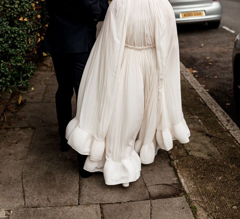 Bride in a Lanvin wedding dress and long sleeve bridal cape with ruffle hem walking through London with her husband 