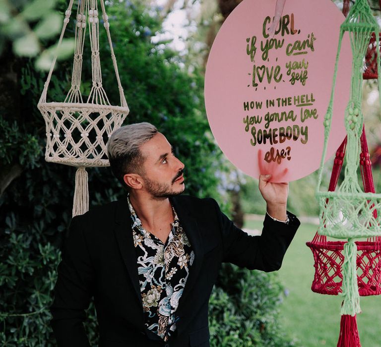 Groom points to a sign that reads 'Gurl, if you can't love yourself how in the hell are you going to love anybody else.'. Photography by Stephanie Shenton.