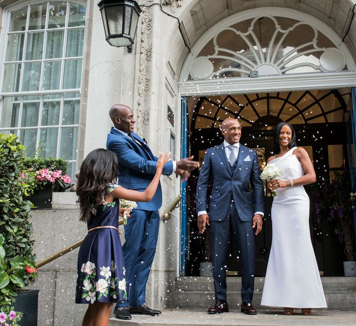 Bride in a fitted Roland Mouret dress standing on the steps of Chelsea Town Hall with her husband in a navy suit