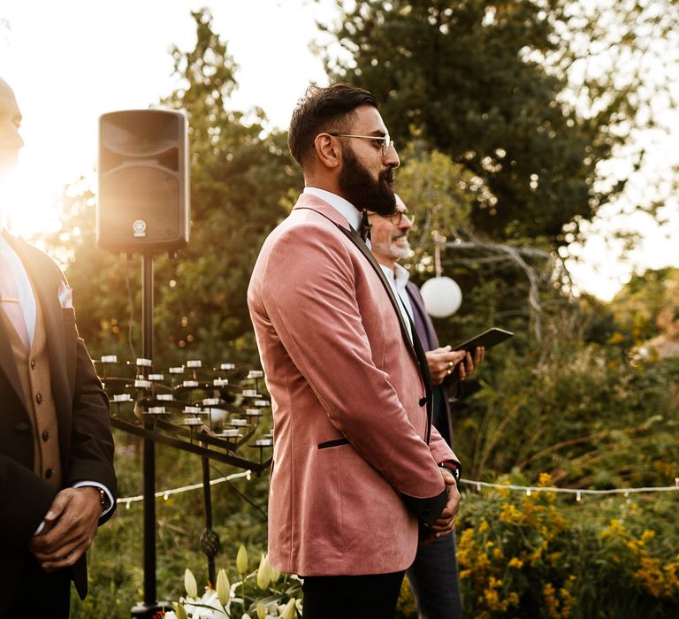 Groom wears pink Topman suit whilst stood outside 