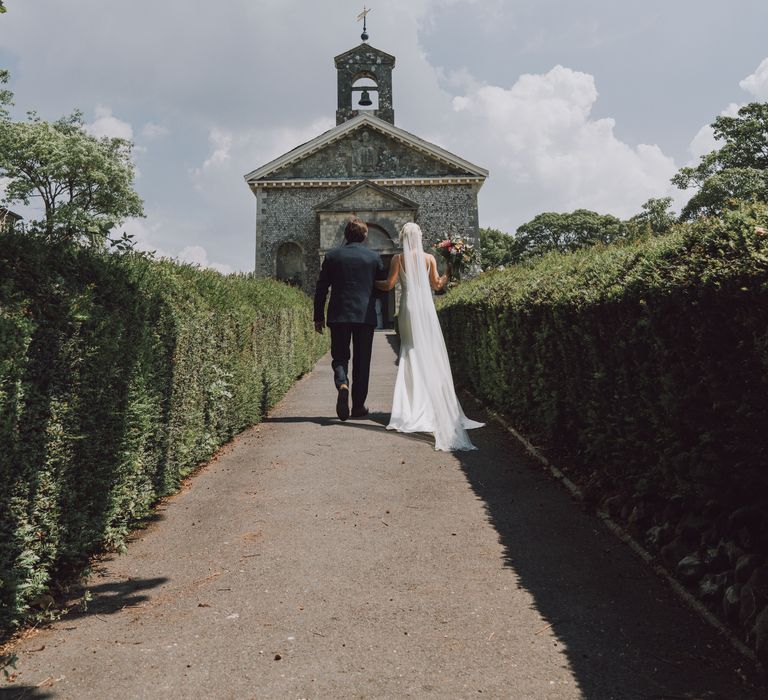 Bride walks with her father to the church whilst holding colourful and bright bouquet