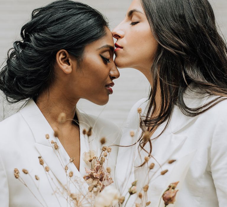 Bride kissing the other bride on the forehead after their all white wedding ceremony