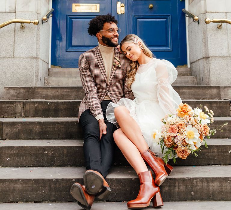 Bride and groom sitting on the steps at Chelsea Town Hall micro wedding in a brown check blazer and short wedding dress