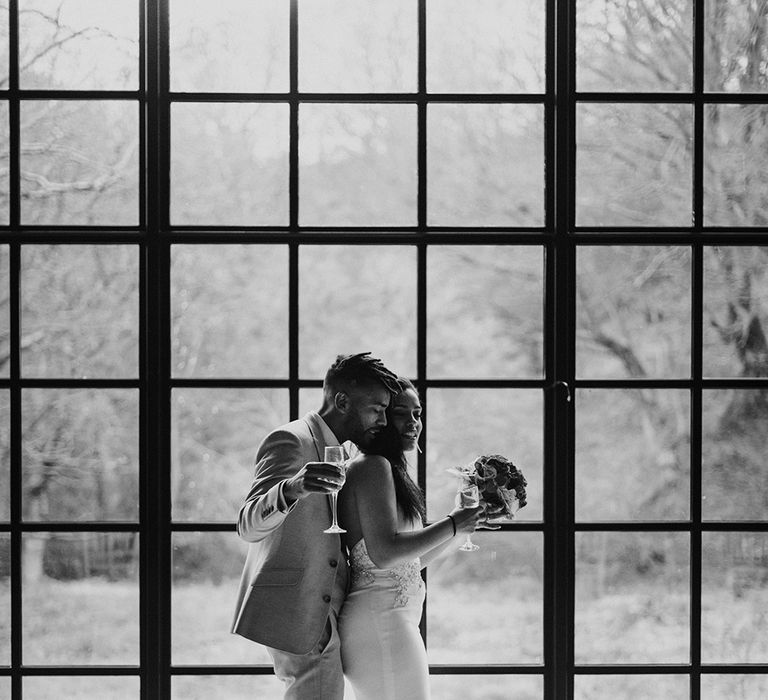 Black & white image of bride & groom dancing on their wedding day in front of arched window