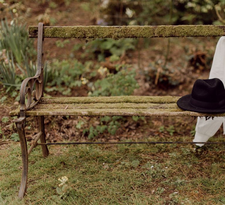 Black fedora and white blouse resting on bench outside at garden party wedding in Devon