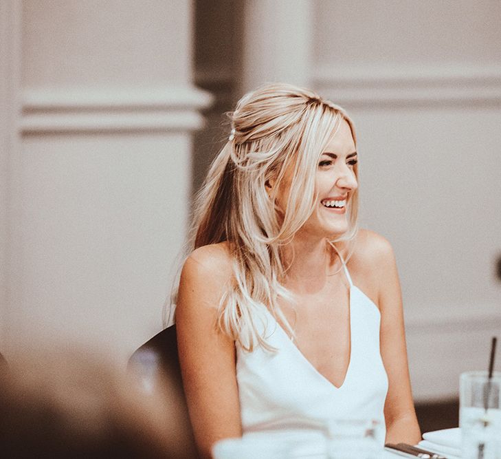 Bride in a Dove Grace Loves Lace wedding dress with half up half down wedding hairstyle laughing during the wedding reception speeches 