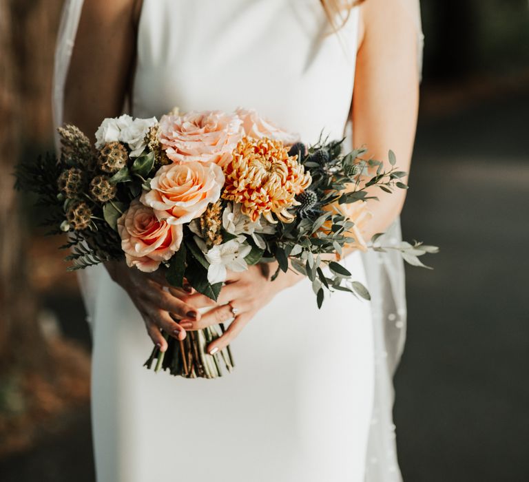 Bride holds peach coloured bouquet complete with green foliage