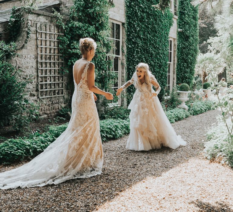 Two brides engage in a 'first look' before their wedding ceremony. They are laughing with mouths open.