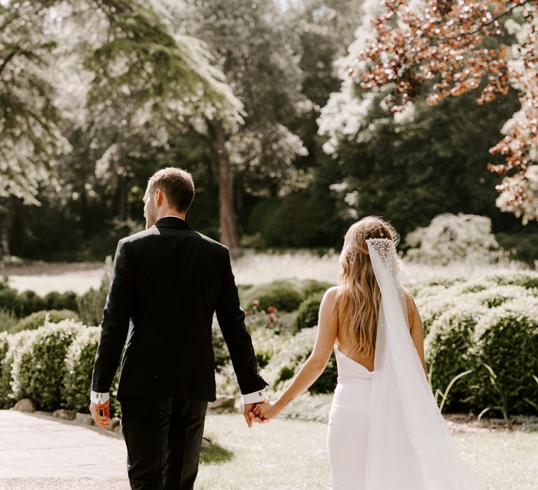 Bride & groom walk hand in hand on their wedding day as the sun shines