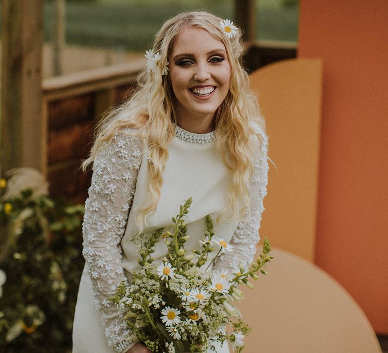 Sixties bride in a mini wedding dress with long wavy hair and wildflowers holding a daisy bouquet 