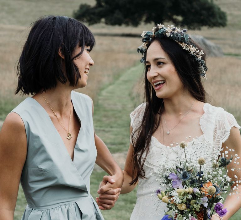 Bride stands with bridesmaid who wears modern bridesmaid gown in sage green 