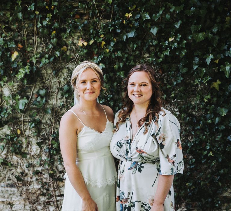 Bride stands with her bridesmaid on her wedding day, bridesmaid wears floral dress 