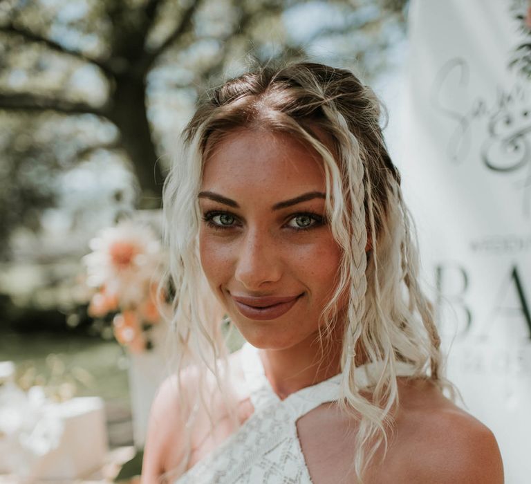 Smiling bride with blond beach waves and plaits wearing lace halter neck boho wedding dress stands outside for birds of paradise wedding inspiration