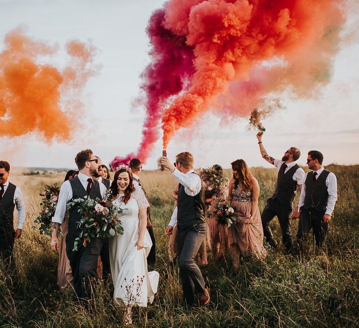 Wedding party smoke bomb portrait in a field with the groomsmen in waistcoats holding red and orange smoke grenades 