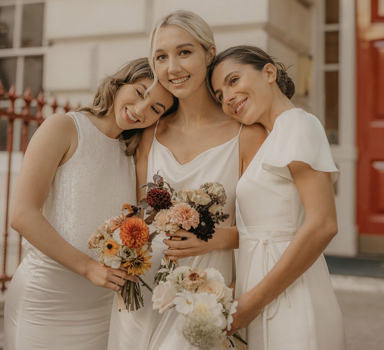 Bridesmaids in white satin dresses holding orange autumn wedding bouquets with pom pom dahlias