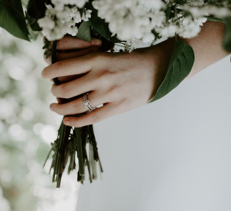 Bride holds floral bouquet complete with white flowers and wears square diamond surrounded by smaller diamonds 