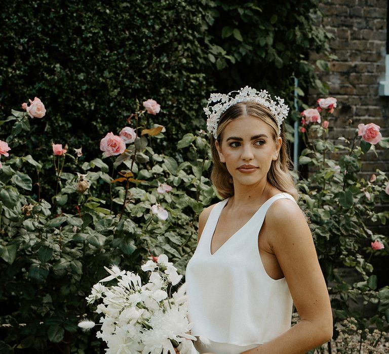 Bride in a white satin slip wedding dress with layered top and front split and white flower crown holding a white wedding bouquet 