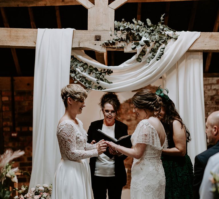 Wedding ceremony at Woolas Barn with two brides exchanging rings in an appliqué wedding dress and embellished gown 