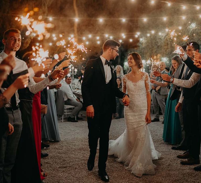 Bride & groom walk underneath fairy light canopy as wedding guests stand around them | Royal Studio