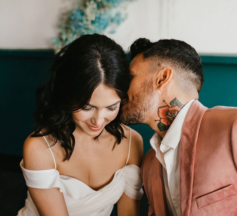 Groom in a pink velvet jacket with neck tattoo kissing his brides neck in a cold shoulder wedding dress 