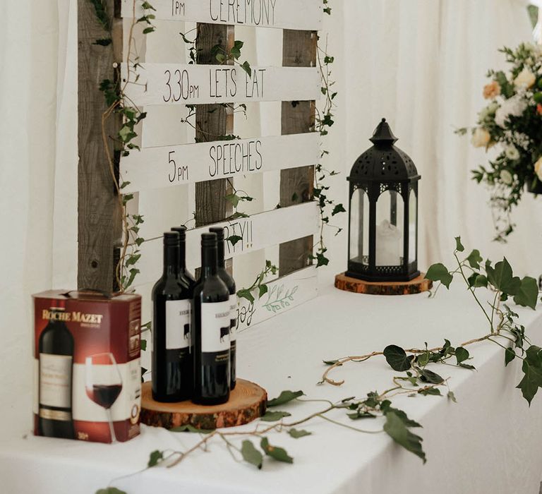 DIY order of day on pallet painted white and surrounded by green foliage