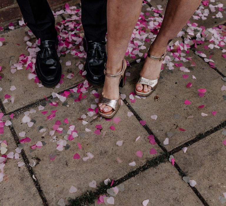 Brides gold platform heels and Grooms tassel black loafers stepping on pink confetti 