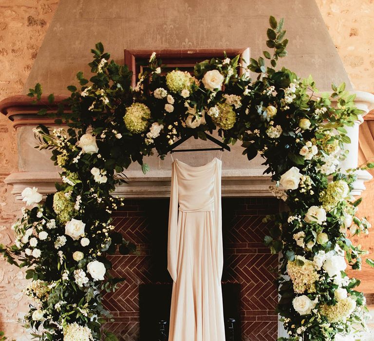 Bridal gown hands between floral archway complete with white florals