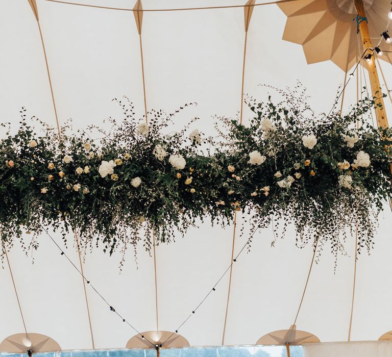 Large green, white and peach flower cloud hanging from ceiling of rustic tent wedding reception 