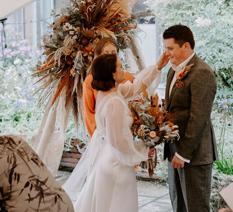 Bride in a long sleeve wedding dress caressing her grooms face during their bespoke ceremony at The Copse Country House 