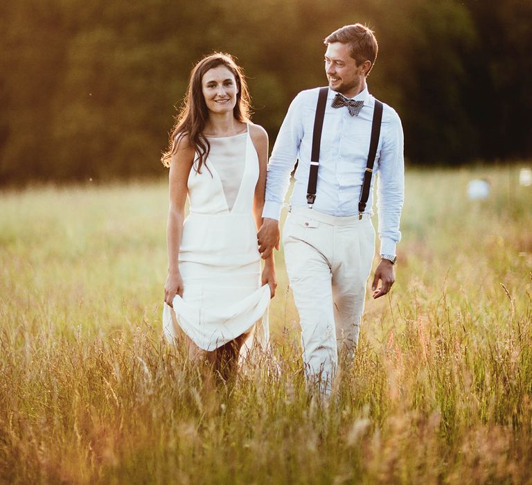 Bride & groom walk in field as the sun begins to set during golden hour