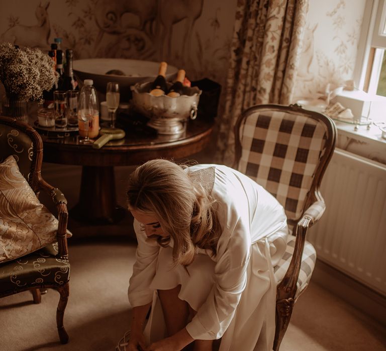 Bride in a satin getting ready robe putting on her pearl Charlotte Mills wedding peep toe wedding shoes 