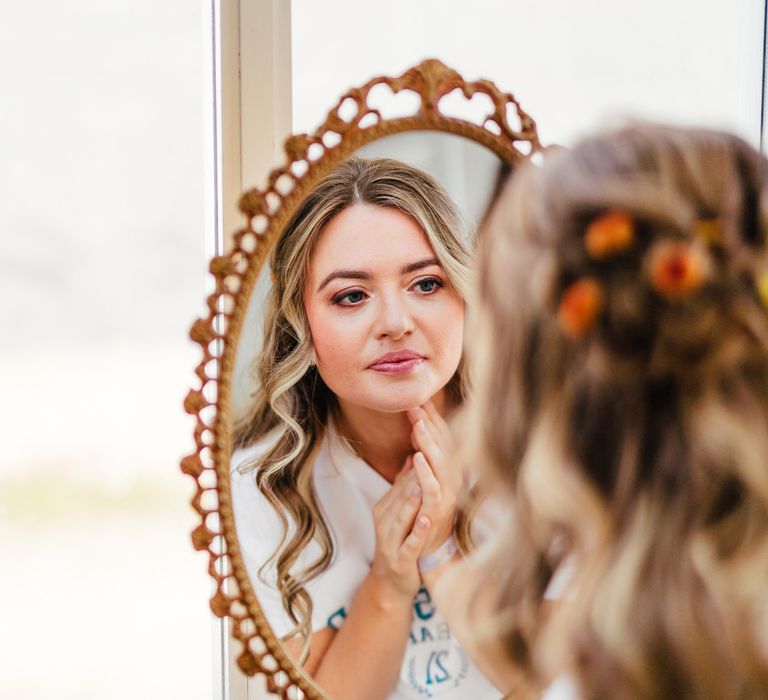 Bridesmaid with curled hair and orange eyeshadow looks in the mirror before wedding