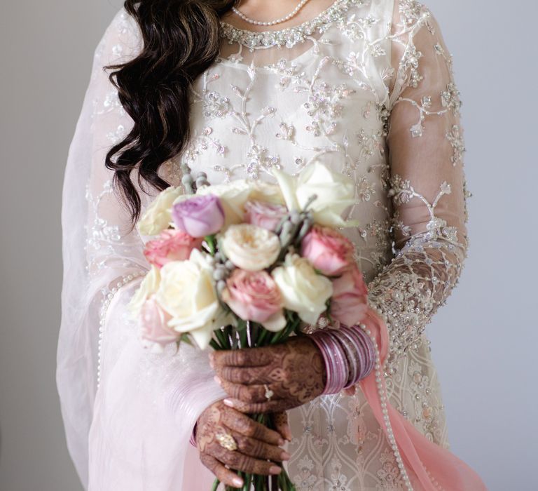 Bride smiles and looks toward camera holding pastel bouquet and wears her dark hair in loose curls 