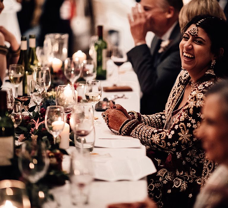 Bride smiles at wedding table with tall wine glasses and sequin jewellery pieces