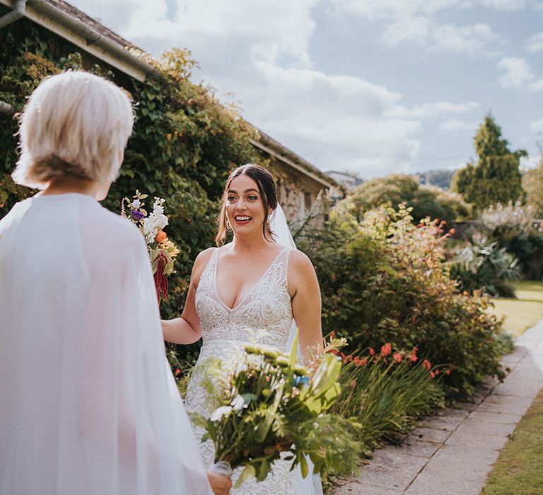 Brides see each other's outfits for their wedding day for the first time with colourful wedding bouquet and cape