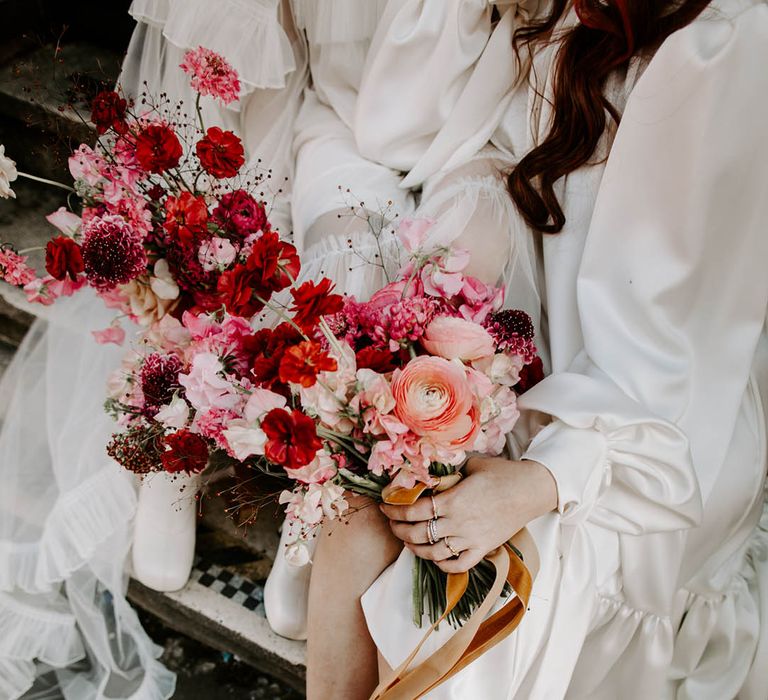 two brides holding red and pink bouquets with sweet peas and butterfly ranculus 