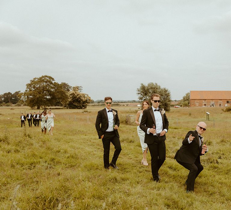 Groomsmen and bridesmaids walk around the wedding venue together with groomsmen doing funny poses 