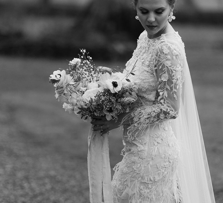 Bride in a long sleeve wedding dress with applique and feather detail and long wedding veil 