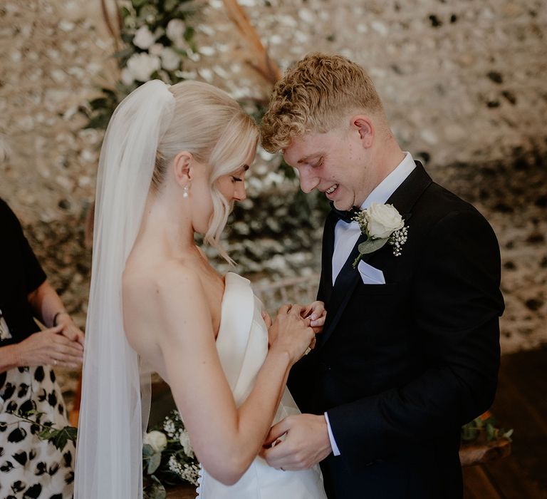 Bride and groom look down at the bride's wedding ring as they are announced ash husband and wife at their barn wedding 