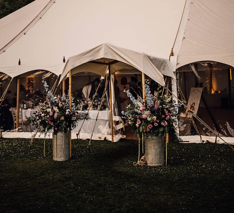 White marquee wedding with the entrance decorated with pink and blue flowers in vintage churns 