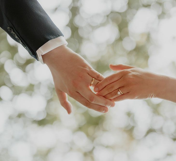 Groom wears gold wedding band and holds brides hand wearing gold wedding band and diamond engagement ring