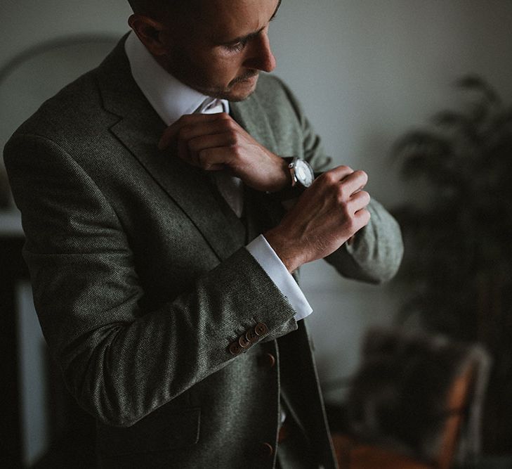 Groom wears three piece suit as he does up his cufflinks on the morning of his wedding day