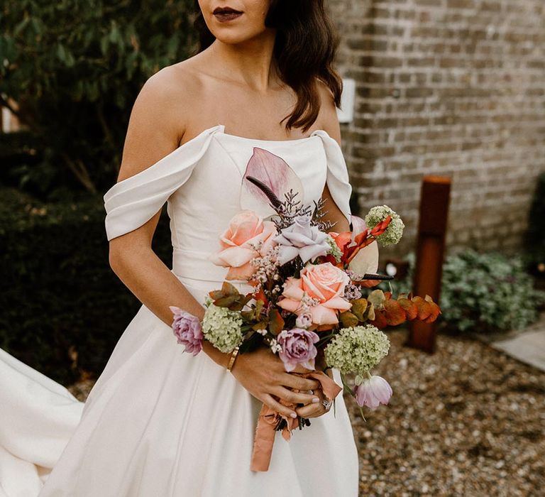 Bride with a dark lip wears an off the shoulder wedding dress holding an autumnal wedding bouquet 