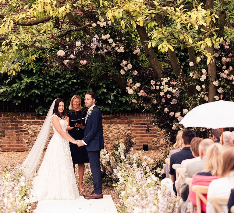 Bride and groom hold hands for their outdoor civil ceremony for their English country garden style wedding 