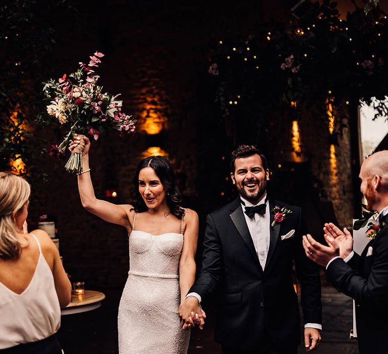 Groom in a classic black tuxedo walks back down the aisle with the bride in a beaded sparkle wedding dress 