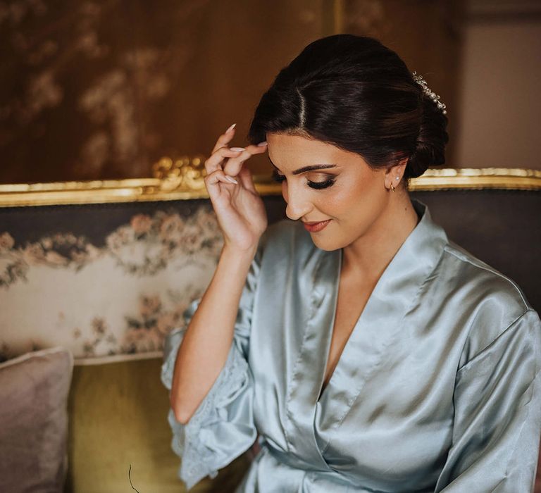 Bride wearing a blue satin robe with dark brown hair and smoky eye makeup holding a white flower bouquet 