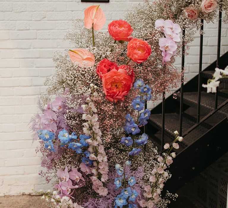 Colourful pink, purple, blue and white gypsophila, anthuriums, peonies, roses, orchids, and dyed grass decorating the staircase at Loft Studios 